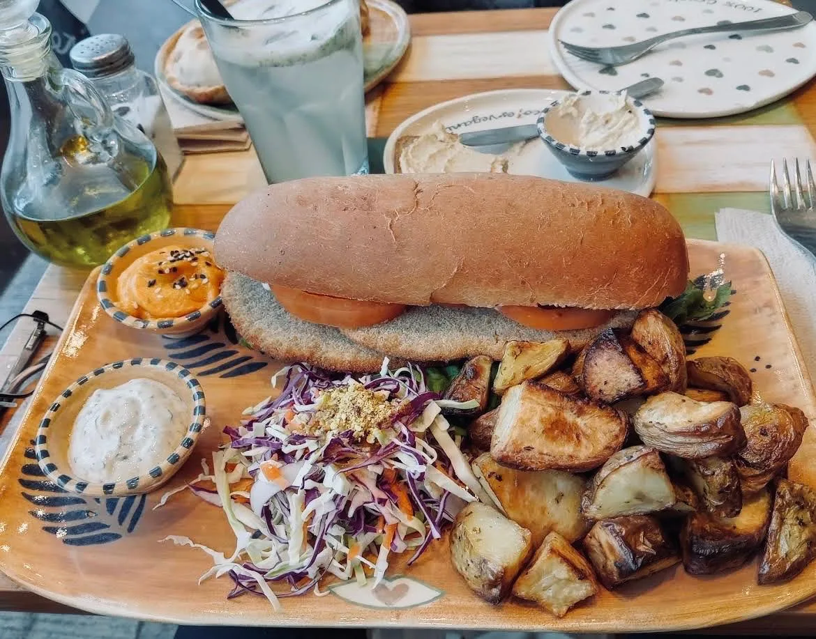 Sándwich vegano en pan casero con coleslaw y papas rústicas en tabla de madera