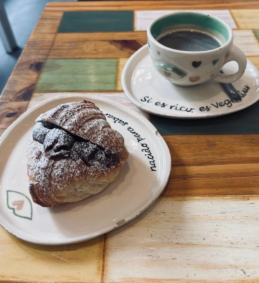 Medialuna rellena de chocolate con azúcar impalpable junto a un café; los platos dicen “Si es rico, es Veganius” y “nacido para salvar animales”